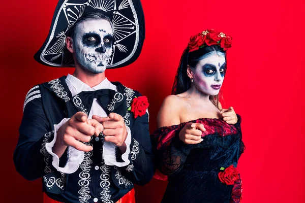 赤い指の上に死んだ衣装のメキシコの日を身に着けている若いカップルは 幸せで面白い顔をしたカメラに指を指しています 良いエネルギーと振動は — ストック写真