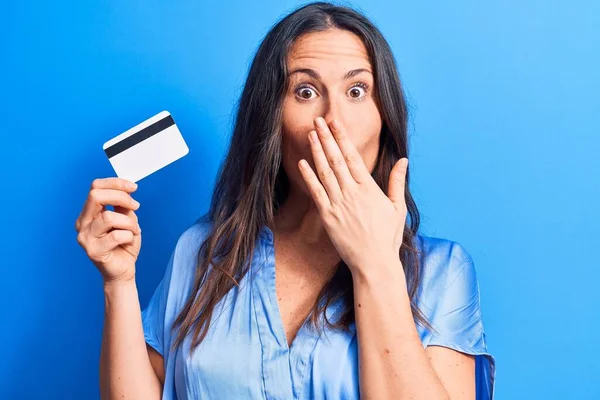 Młoda Piękna Brunetka Trzymająca Kartę Kredytową Odizolowanym Niebieskim Tle Zakrywająca — Zdjęcie stockowe
