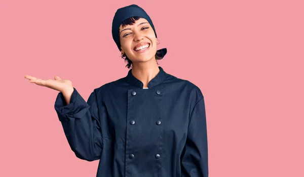 年轻的黑发女子 身穿职业厨师制服 笑容满面 手心朝前看相机 — 图库照片