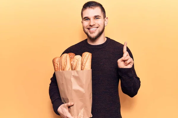 Young Handsome Man Holding Paper Bag Bread Smiling Idea Question — Stock fotografie