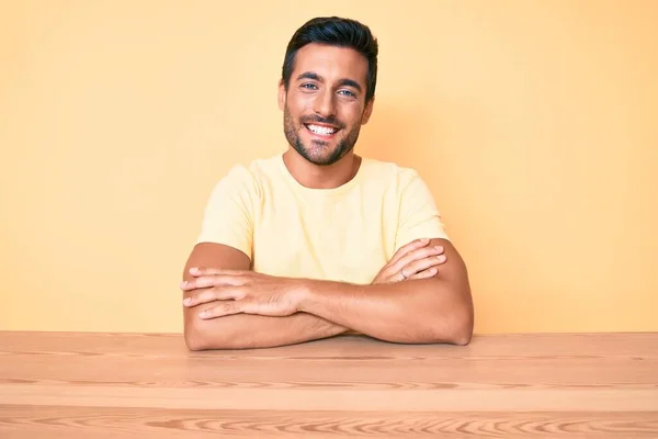 Mladý Hispánec Oblečený Neformálního Oblečení Sedí Stole Usmívá Zkříženýma Rukama — Stock fotografie