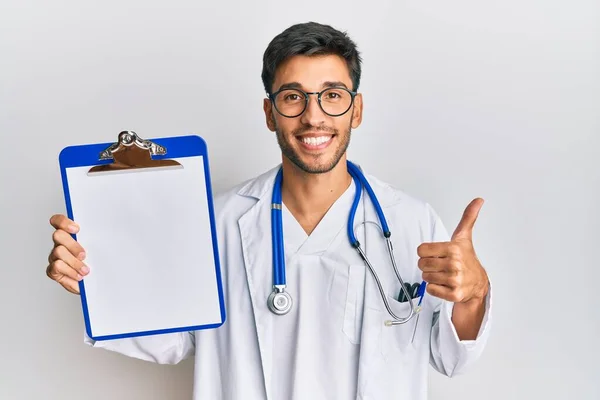 Jovem Homem Bonito Vestindo Estetoscópio Médico Segurando Prancheta Sorrindo Feliz — Fotografia de Stock