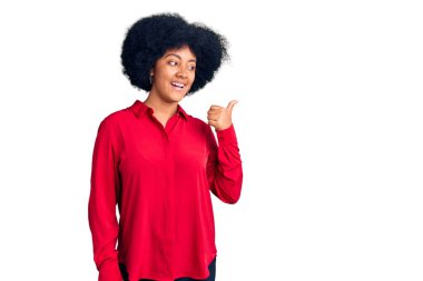 Genç Afro-Amerikan kızı, günlük kıyafetler giyip gülümsüyor, gülümsüyor ve başparmağıyla yan tarafı işaret ediyor.. 