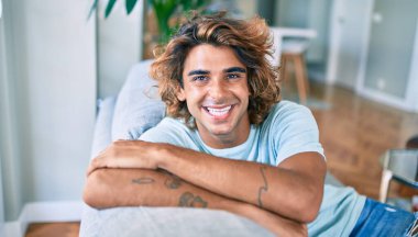 Evdeki kanepede mutlu gülümseyen İspanyol genç adam.