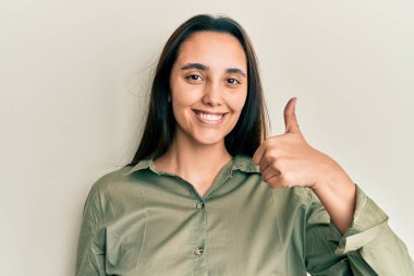 Neşeli ve pozitif gülümseyen Latin kökenli genç bir kadın. Başparmağıyla mükemmel ve onay işareti yapıyor. 