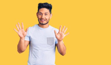 Yakışıklı Latin Amerikalı gündelik giysiler giymiş on numaralı parmaklarıyla onu gösterirken kendinden emin ve mutlu bir şekilde gülümsüyor.. 