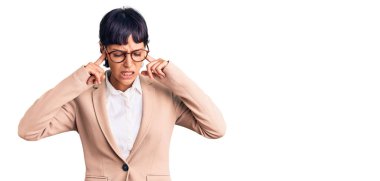 Kısa saçlı, iş ceketi giyen, kulaklarını parmaklarıyla kapatan ve yüksek sesli müzik sesi için rahatsız edici ifadeler takınan esmer bir kadın. sağır kavramı. 