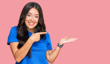 Güzel, esmer, gündelik kıyafetler giyen genç bir kadın kameraya hayret ediyor ve gülümsüyor.. 