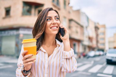 Genç İspanyol kadın gülümsüyor. Akıllı telefonla konuşuyor ve şehirde kahve içiyor..