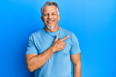 Orta yaşlı, gri saçlı, günlük kıyafetler giyen, neşeli, yüzünde mutlu ve doğal bir ifadeyle elleri ve parmaklarıyla yüzünü gösteren bir gülümseme olan bir adam. 