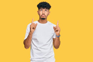 Gündelik beyaz tişört giyen genç Arap adam üzgün ve üzgün görünüyor, parmaklarıyla yönü gösteriyor, mutsuz ve depresif.. 