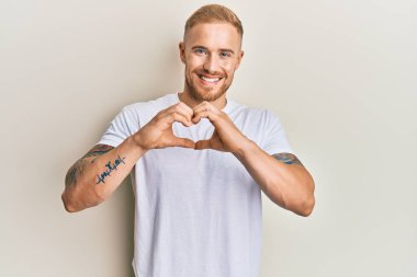 Gündelik beyaz tişört giyen beyaz bir genç aşık gülümsüyor. Elleriyle kalp sembolü yapıyor. romantik kavram. 