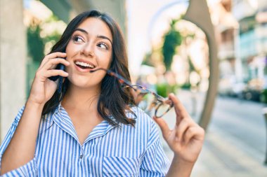 Genç İspanyol iş kadını gülümsüyor. Şehirdeki akıllı telefondan mutlu bir şekilde konuşuyor..