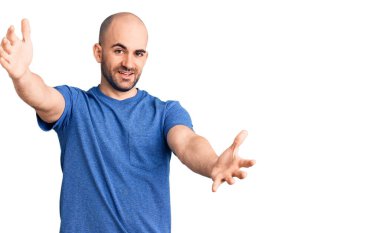 Gündelik tişört giyen genç yakışıklı adam kameraya bakıp sarılmak için kollarını açmış gülümsüyor. Mutluluğu kucaklayan neşeli bir ifade.. 