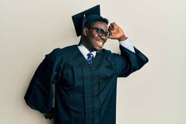 Mezuniyet şapkası ve tören cübbesi giyen yakışıklı siyahi adam. Yorgun ve rahat, uykulu ve sabahın erken saatleri için esniyor. 