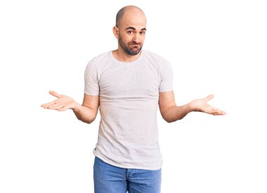 Sıradan tişörtler giyen, elleri ve kolları havada, kafası karışık genç ve yakışıklı bir adam. şüphe kavramı. 