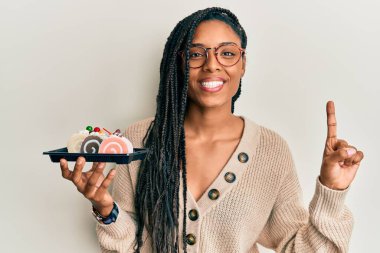 Elinde pasta tatlısı tutan Afrikalı Amerikalı bir kadın bir fikirle ya da soruyla gülümsüyor ve mutlu bir yüzle işaret ediyor. 