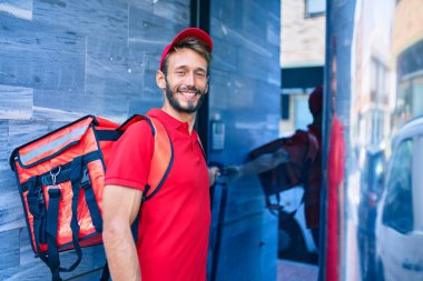 Beyaz teslimatçı, kırmızı üniforma giyiyor ve sırt çantası teslim ederken gülümsüyor.