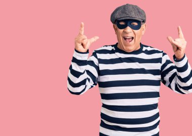 Hırsız maskesi ve tişört giyen yakışıklı adam çılgın bir ifadeyle bağırıyor elleri havada rock sembolü yapıyor. Müzik yıldızı. ağır müzik konsepti. 