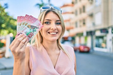 Genç sarışın kadın gülümsüyor. Yeni Zelanda 'yı mutlu ediyor. Şehirde 100 dolarlık banknotlar tutuyor..