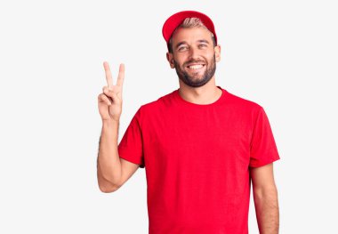 Tişört ve şapka giyen yakışıklı genç adam iki numaralı parmaklarıyla kendini beğenmiş ve mutlu gülümserken kendini gösteriyor.. 