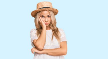 Yazlık şapka takan genç sarışın kız kollarını kavuşturup depresyondan sıkılmış ve yorgun görünüyor.. 