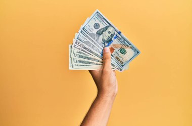 Amerikan dolarlarını izole edilmiş sarı arka planda tutan İspanyol bir adamın eli..