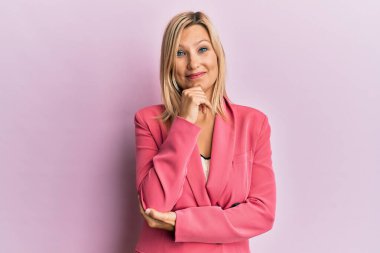 Orta yaşlı, beyaz, iş ceketi giyen, çenesi üstünde soru soran, düşünceli bir kadın. Düşünceli bir yüzle gülümsüyor. şüphe kavramı. 