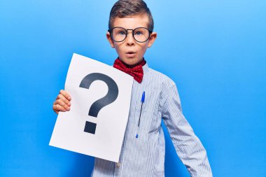 Sevimli sarışın çocuk inek papyonu takıyor ve gözlük takıyor. Soru işareti taşıyor. Şaşırmak için ağzı açık ve korkmuş. 