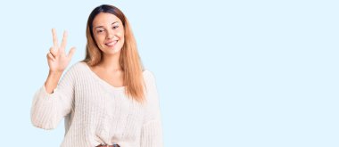 Güzel, genç bir kadın gündelik kıyafetler giyer ve üç numarayı göstererek gülümserken kendinden emin ve mutluydu.. 