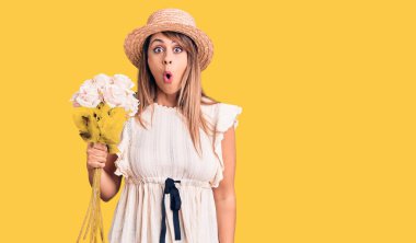 Şapka takan güzel bir kadın elinde bir buket çiçekle şaşırmış ve şaşırmış bir şekilde ağzı açık kalmış, inançsız bir yüz. 