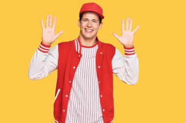 Beyzbol üniforması giyen yakışıklı beyaz adam on numarayı gösterip işaret ederken kendinden emin ve mutlu bir şekilde gülümsüyor.. 