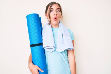 Güzel, beyaz bir kadın yoga minderi tutuyor. Korkmuş ve ağzı açık kalmış, şaşırmış ve şaşırmış. 