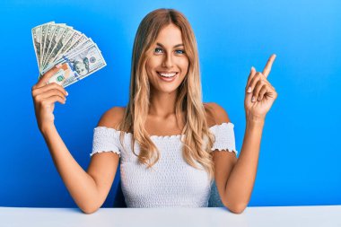 Dolarları tutan güzel sarışın genç kadın mutlu bir şekilde elini ve parmağını kenarda gezdiriyor. 