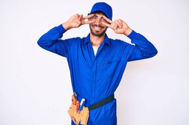 Kıvırcık saçlı ve ayı gibi giyinen yakışıklı genç adam barış sembolü yapıyor. Yüzünde parmaklar, gülümseyerek zaferi gösteriyor. 