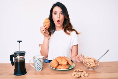 Genç, güzel, esmer bir kadın kahvaltı yapıyor elinde kruvasan var. Korkmuş ve şaşkın bir şekilde ağzı açık, inançsız bir yüz. 