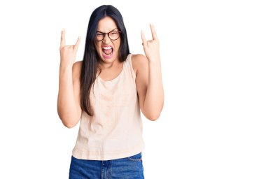 Gündelik kıyafetler ve gözlük takmış, çılgın bir ifadeyle bağıran, elleri havada rock sembolü yapan güzel beyaz bir kadın. Müzik yıldızı. ağır kavram. 