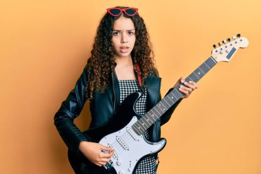 Şok olmuş yüzüne elektro gitar çalan genç İspanyol kız şüpheci ve alaycı görünüyor, ağzı açık kalınca şaşırıyor. 