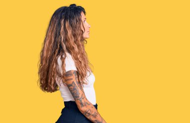 Dövmeli, beyaz tişörtlü, rahat bir görünüm takınan, kendine güvenen gülümseyen İspanyol bir kadın.. 