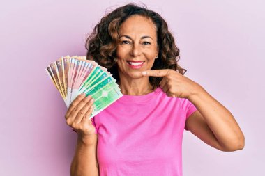 Orta yaşlı İspanyol kadın elinde Norveç kronu banknotları tutarken mutlu mesut parmakla işaret ediyor. 