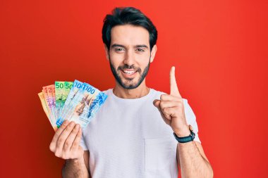 İspanyol asıllı genç adam elinde İsviçre frangı banknotları tutarken bir fikir veya soruyla gülümsüyor ve mutlu bir yüzle işaret ediyor. 