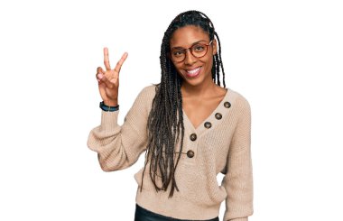 Afro-Amerikalı kadın, günlük giysiler içinde kameraya bakıp parmaklarını zafer işareti yaparken gösteriyor. İki numara.. 