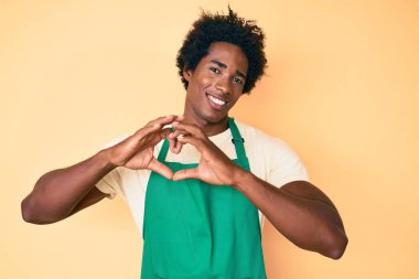 Yakışıklı Afro saçlı, garson önlüğü takan, kalbi ve elleri ile şekillenen, aşık bir şekilde gülümseyen Afrikalı Amerikalı. romantik kavram. 