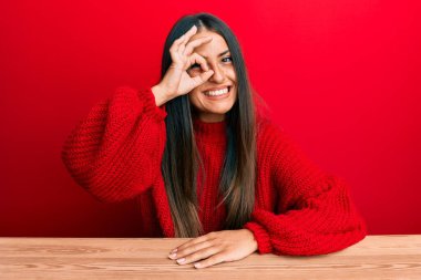 Güzel İspanyol kadın, gündelik giysiler içinde masada oturuyor. El hareketleriyle gülümsüyor, gözleriyle mutlu yüzüyle parmaklarının arasından bakıyor.. 