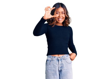 Genç, güzel, melez bir kadın, günlük kıyafetler giymiş, gülümseyen, kendine güvenen, el hareketleriyle hareket eden, parmaklarıyla işaret eden ve kameraya bakan. ölçüm kavramı. 