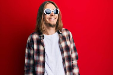 Uzun saçlı, hippi tişörtü giyen, güneş gözlüğü takan, rahat bir görünüm takınan, kendine güveni olan yakışıklı beyaz bir adam.. 