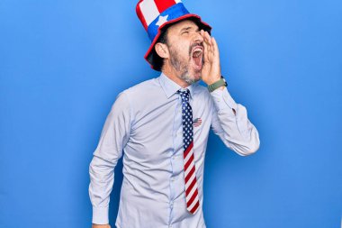 Orta yaşlı, yakışıklı, vatansever, şapkalı ve kravatlı bir adam mavi arka planda avazı çıktığı kadar bağırıyor. İletişim konsepti.