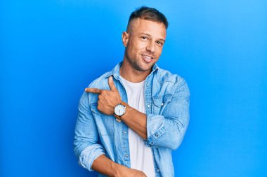 Yakışıklı, sıradan bir kot ceket giyen, eli ve parmağı yanda gülümseyen kaslı adam. 