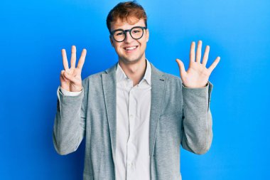 Zarif kıyafetler giyen, gözlüklü genç beyaz adam sekiz numaralı parmaklarını göstererek gülümseyerek kendinden emin ve mutlu görünüyor.. 