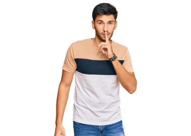 Gündelik kıyafetler giyen genç yakışıklı adam parmakları dudaklarında sessiz olmak istiyor. sessizlik ve gizli konsept. 